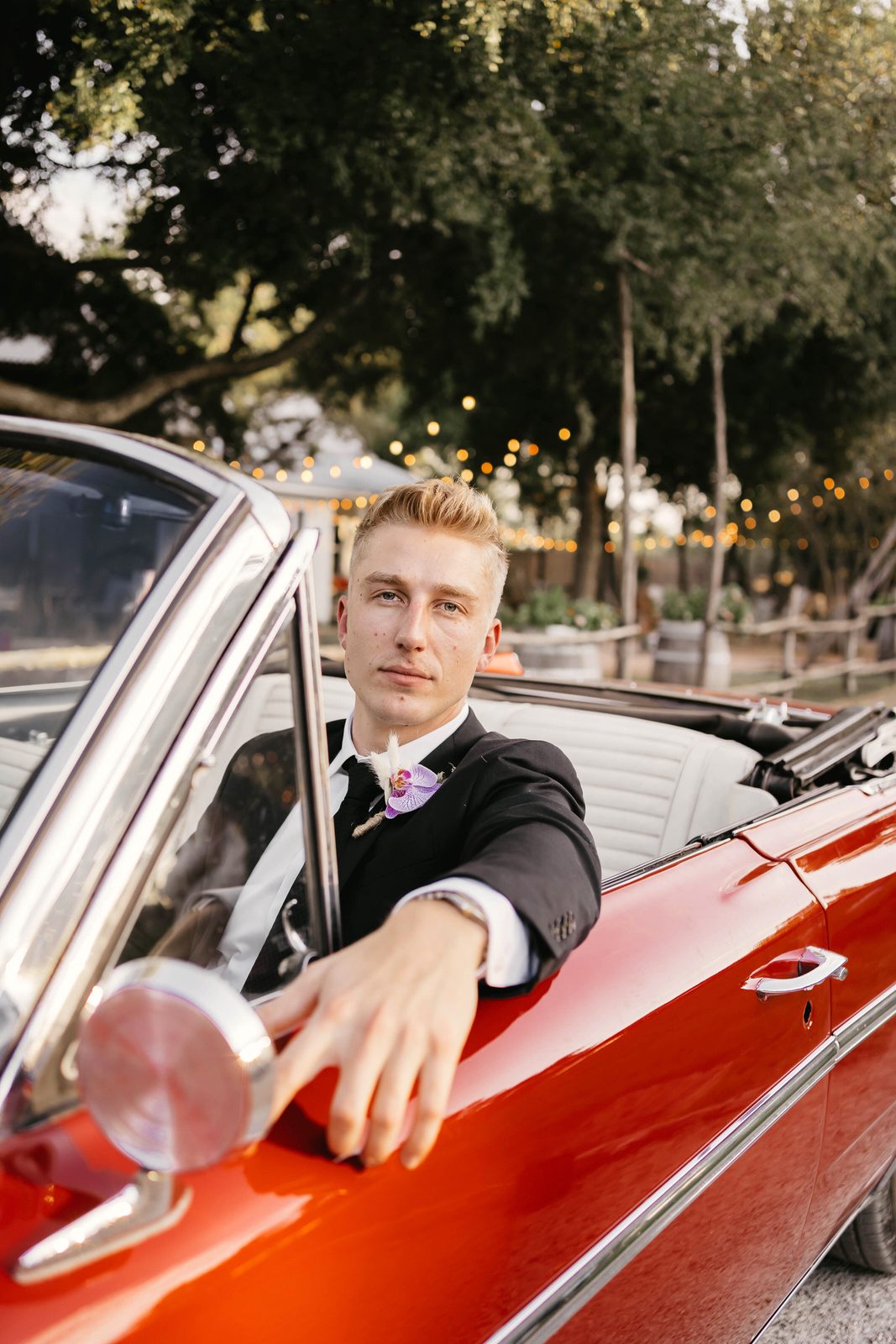 A groom leaning out of a vintage red convertible at The Chapel at Gruene